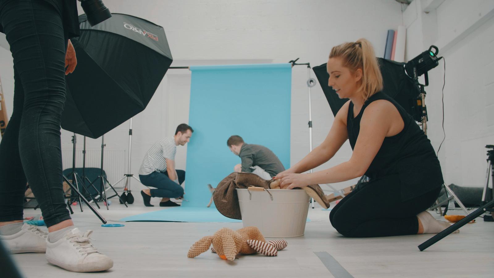 Nomadic UK - stylist setting up a look on a video shoot in a studio with a blue backdrop